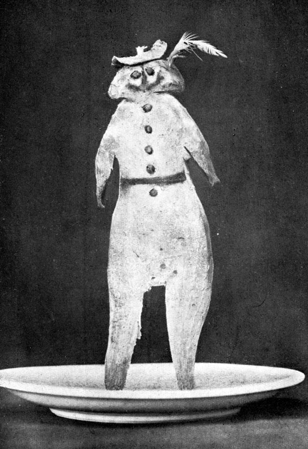 Fotografia czarno-biała. Kadr przedstawiający figurkę podkoziołka postawioną na białym talerzyku.